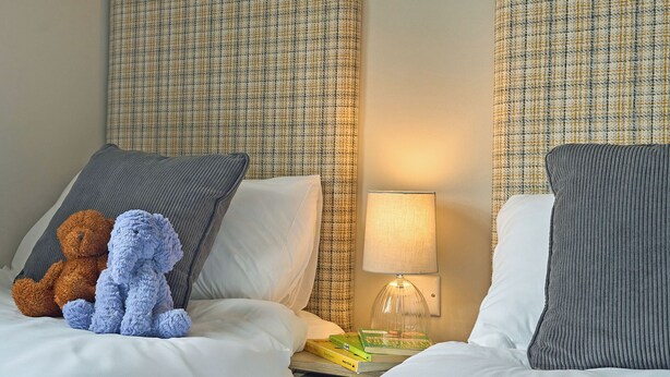 Ein Hotelzimmer mit zwei Betten, einem Nachttisch mit Lampe und einem Teddybären auf einem Bett.
