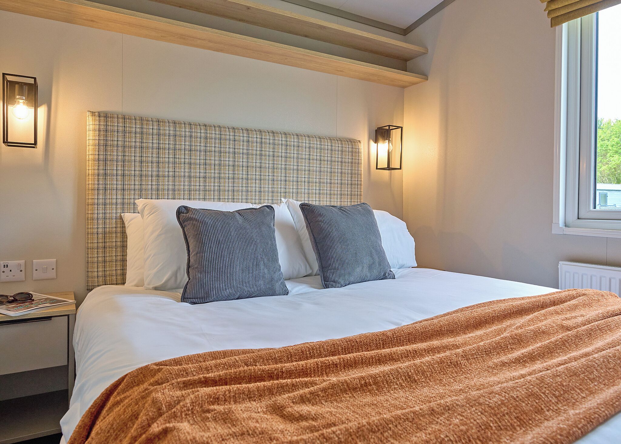 A hotel room with a bed, headboard, bedside lamps, and a window.