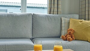 Ein graues Sofa mit einem Teddybär und zwei Gläsern Orangensaft auf einem Holztisch.