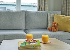 A grey sofa with a teddy bear and two glasses of orange juice on a wooden table. - Luxury 3 bedroom Hot Tub sleeps 8 (Hayle)