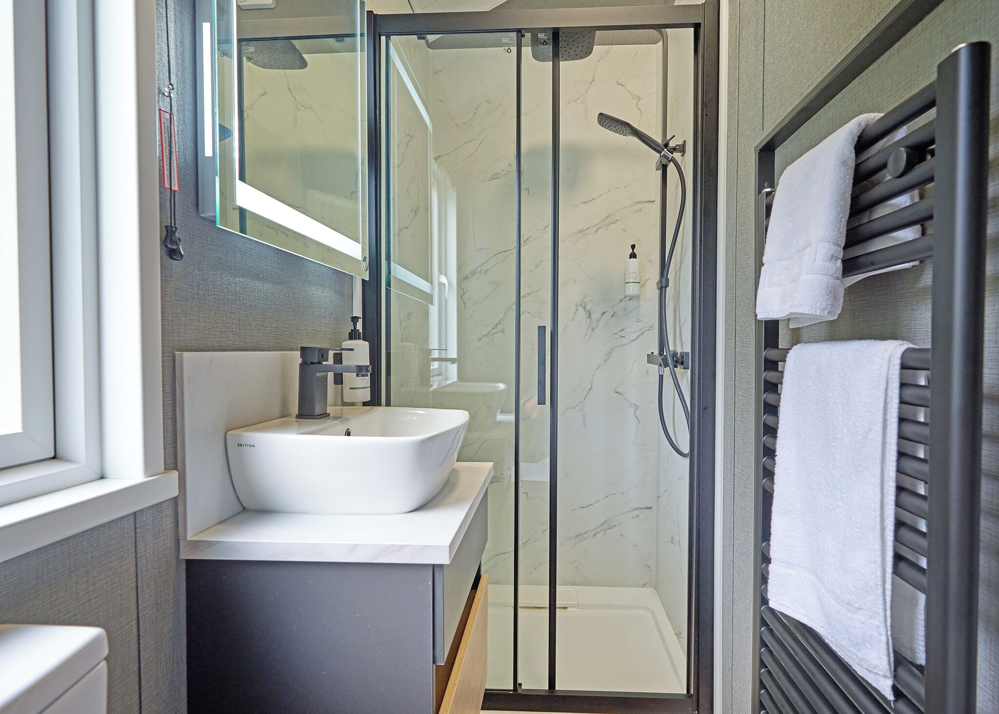 Ein modernes Badezimmer mit einer begehbaren Glasdusche, einem weißen Waschbecken und einem Handtuchhalter.