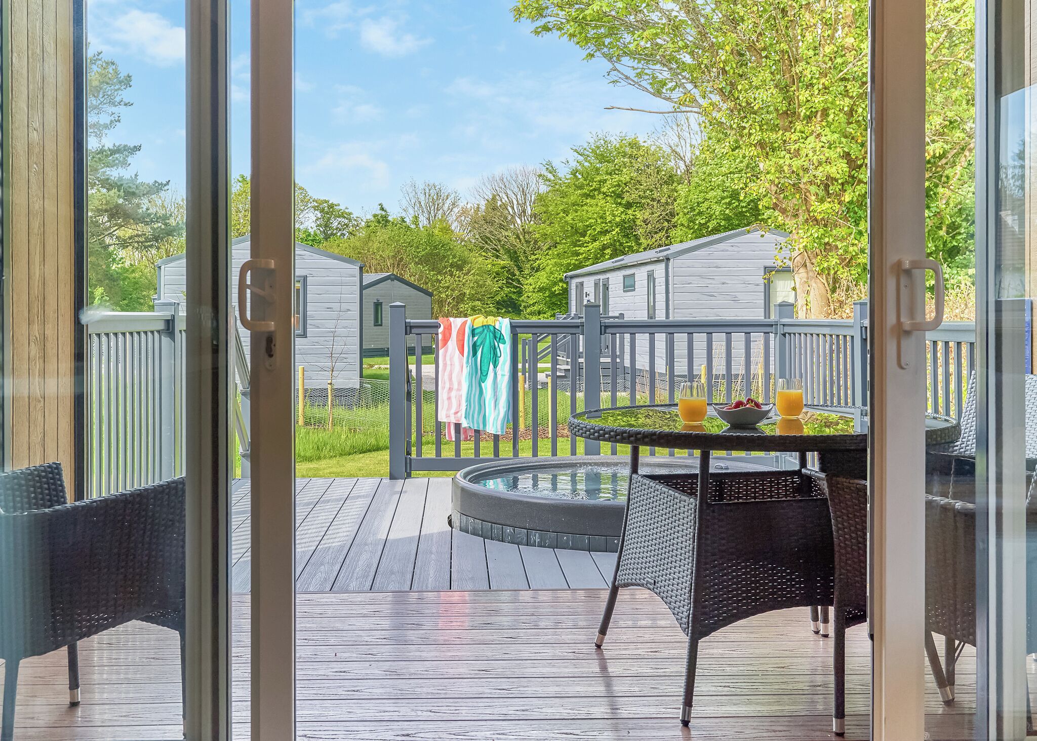 A deck with a table and chairs, a hot tub, and a view of a residential area with houses and trees.