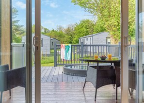 A deck with a table and chairs, a hot tub, and a view of a residential area with houses and trees. - Glamping Pods with hot tubs (Hayle)