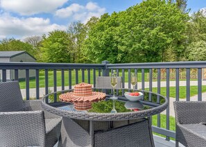 A round outdoor table with wicker chairs, a wicker basket, a bowl of strawberries, and two glasses of white wine on a deck with a railing. - Luxury 3 bedroom sleeps 8 Pet Friendly (Hayle)
