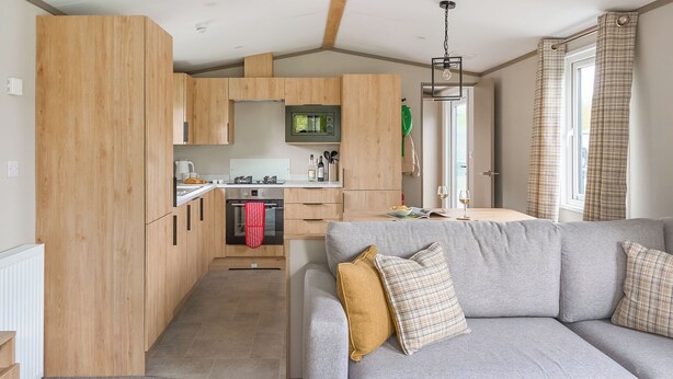 Una cocina moderna con armarios de madera, microondas integrado y un comedor con sofá gris.