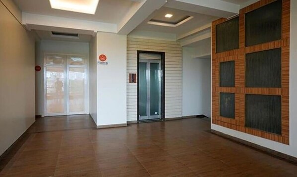 A hallway with a wooden floor, a glass elevator, and a wall with a patterned design. - Rester Select Chakan (Rajgurunagar)