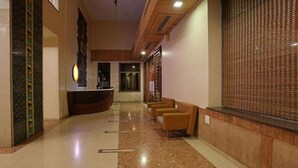 A hotel lobby with a reception desk, a waiting area with chairs, and a patterned wall. - Rester Select Chakan (Rajgurunagar)