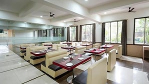 A modern restaurant with booths and tables, large windows, and ceiling fans. - Rester Select Chakan (Rajgurunagar)