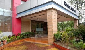 A hotel entrance with a covered walkway, a name sign, and surrounding greenery. - Rester Select Chakan (Rajgurunagar)