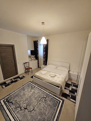 A bedroom with a bed, a chair, a desk, and a hanging light fixture.