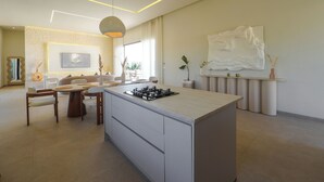 Een moderne keuken met een centraal eiland, een eetgedeelte met een ronde tafel en een zithoek met een bank en een groot abstract schilderij.