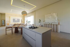 Eine moderne Küche mit einer zentralen Kochinsel, einem Essbereich mit rundem Tisch und einem Wohnbereich mit Sofa und einem großen abstrakten Gemälde.