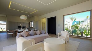 Een moderne woonkamer met een bank, stoelen, een salontafel en een groot raam met uitzicht op groen.