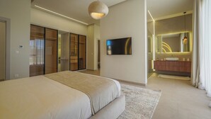 Een moderne slaapkamer met een groot bed, een televisie, een badkamer met spiegel en wastafel, en een inloopkast.