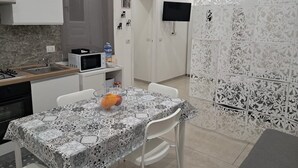 Een kleine keuken met een magnetron, spoelbak en fornuis. Een eettafel met een geruit tafelkleed en stoelen staat in het midden.