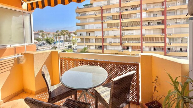 Un balcone con mobili in vimini, un tavolino in vetro e vista su un edificio a più piani.