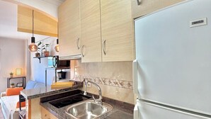 Una cucina moderna con pensili in legno chiaro, un lavello in acciaio inox e un frigorifero Zanussi.