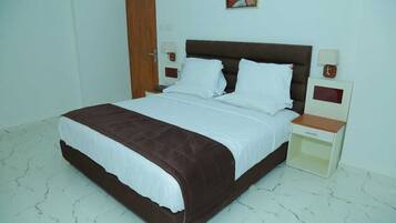 A bedroom with a large bed, two bedside tables, a nightstand, a wall clock, and a door.