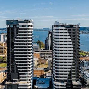 Two modern high-rise buildings with a view of a body of water and distant hills.