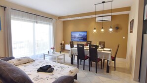 A hotel room with a bed, a dining area with chairs and a table, a TV on the wall, and a balcony with curtains. - Umag flat with terrace and garden (Umag)