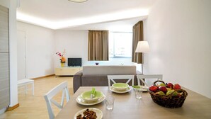 Una habitación de hotel moderna con zona de comedor, cama y televisión.