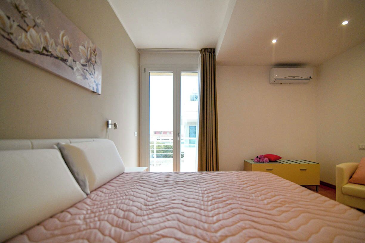 Une chambre d’hôtel avec un grand lit, une commode jaune, une chaise et un tableau accroché au mur.