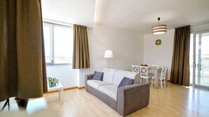 Una sala de estar moderna con un sofá gris, una mesita blanca y un comedor con una mesa y sillas blancas.