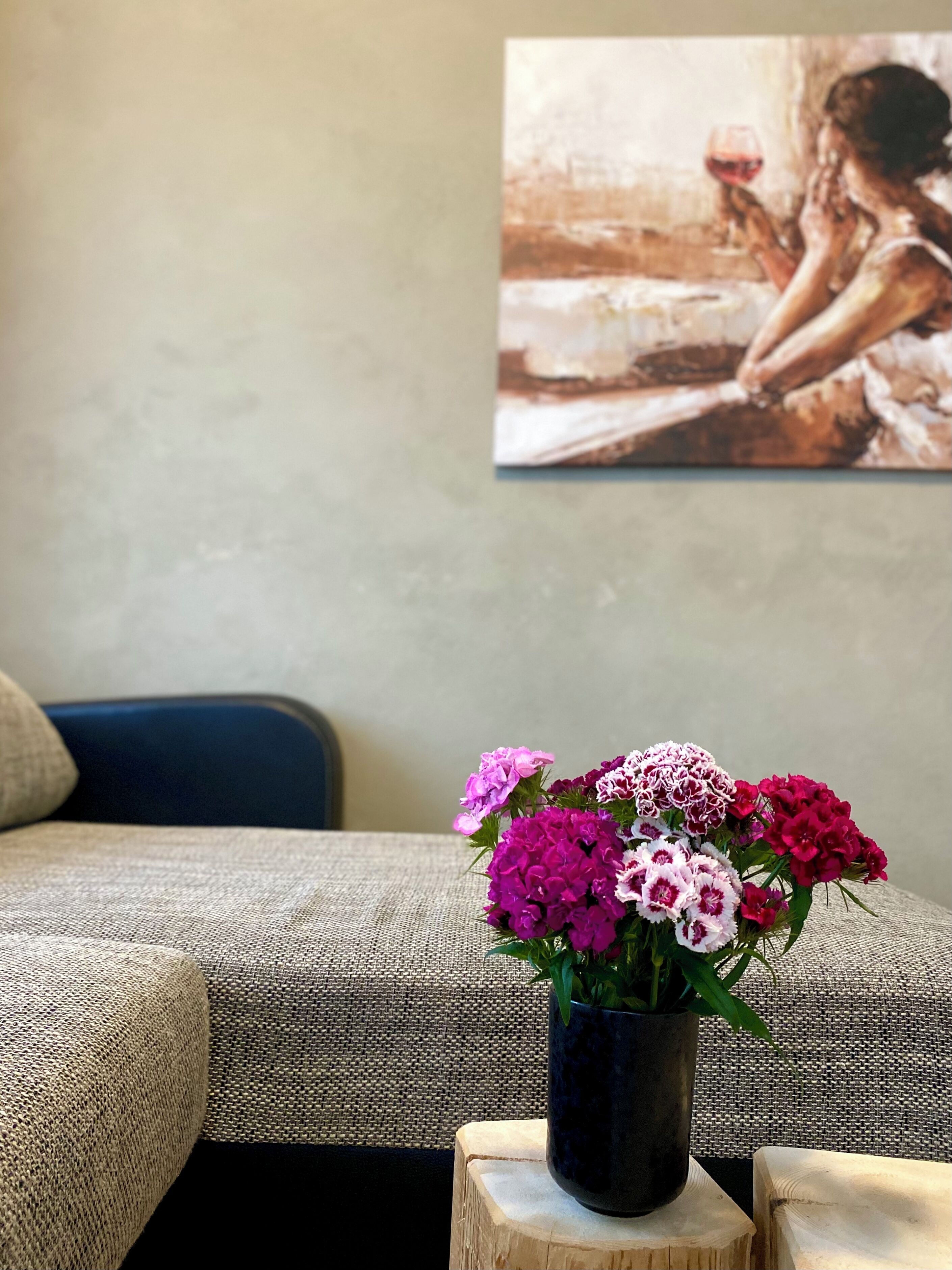A room with a sofa, a small wooden stool, and a vase of flowers.