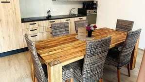 A modern kitchen with wooden cabinets, a black countertop, and a dining area with a wooden table and woven chairs. - Villetta Moscal- „BuonGusto“ (Affi)