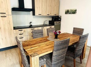A modern kitchen with wooden cabinets, a black countertop, and a dining area with a wooden table and woven chairs. - Villetta Moscal- „BuonGusto“ (Affi)