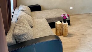 A living room with a sectional sofa, a painting on the wall, and a small wooden table with flowers. - Villetta Moscal- „BuonGusto“ (Affi)