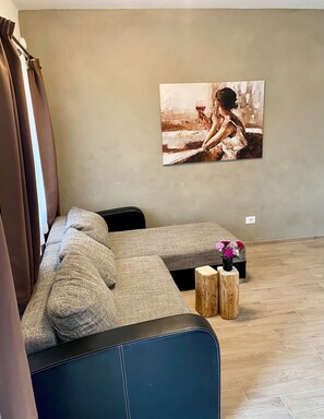 A living room with a sectional sofa, a painting on the wall, and a small wooden table with flowers. - Villetta Moscal- „BuonGusto“ (Affi)