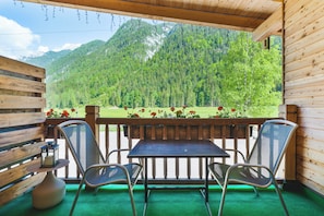 A wooden deck with a table and chairs, overlooking a mountainous landscape with a view of a green field and trees.