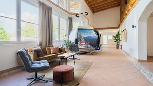 A spacious room with a modern sofa, a small table, a cushioned ottoman, a large window, and a wall-mounted TV. - Mountain View Deluxe: enjoy mountain views together, a balcony, and alpine luxury. Perfect for a romantic stay in summer or winter. (Leutasch)