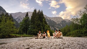 A group of people sitting around a campfire on a rocky riverbank with mountains in the background. - Mountain View Deluxe: enjoy mountain views together, a balcony, and alpine luxury. Perfect for a romantic stay in summer or winter. (Leutasch)