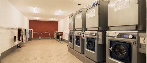 A laundry facility with multiple washing machines, a drying rack, and a folding station.