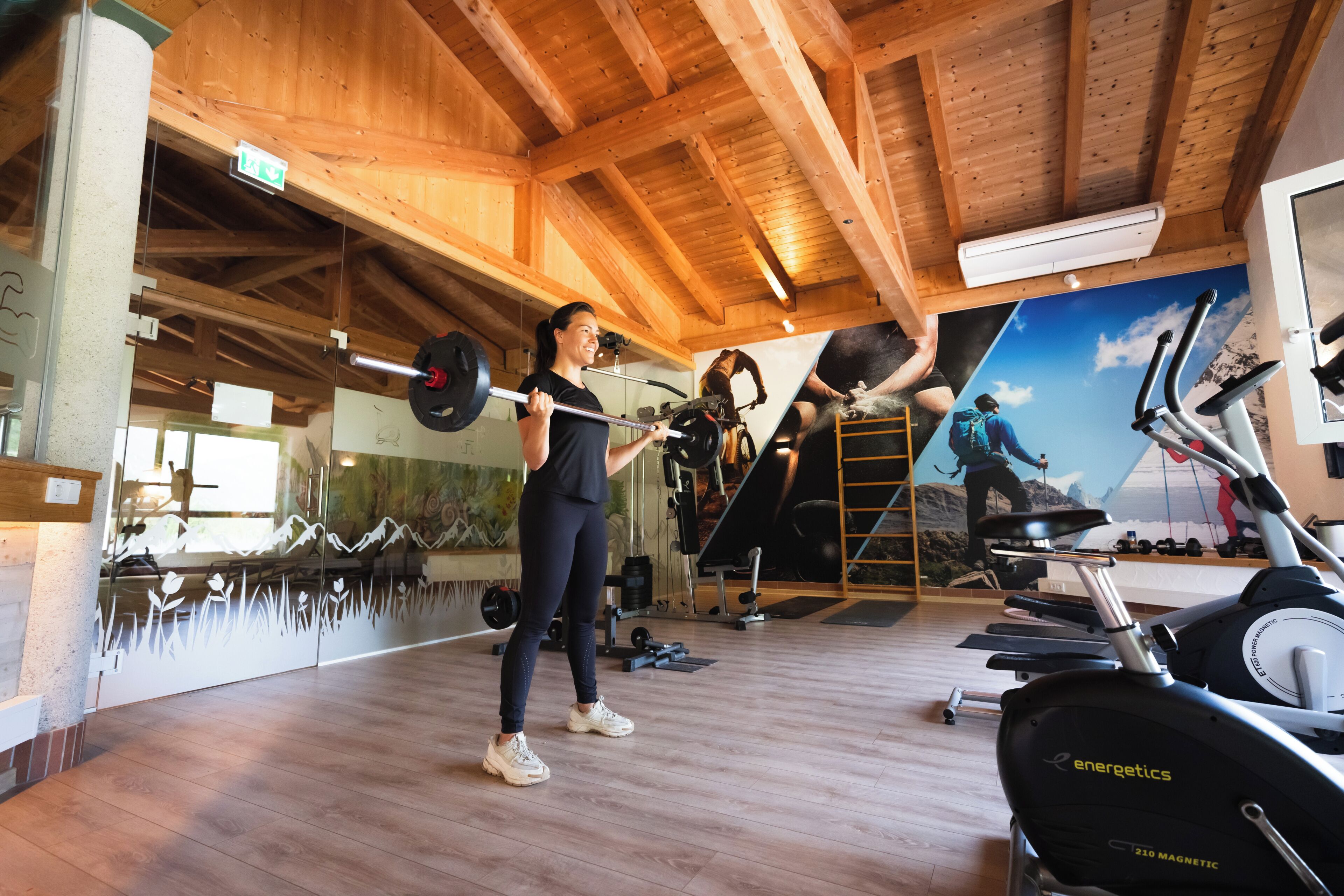 Een sportschool met houten balken, trainingsapparatuur en een muurschildering van natuurlandschappen.