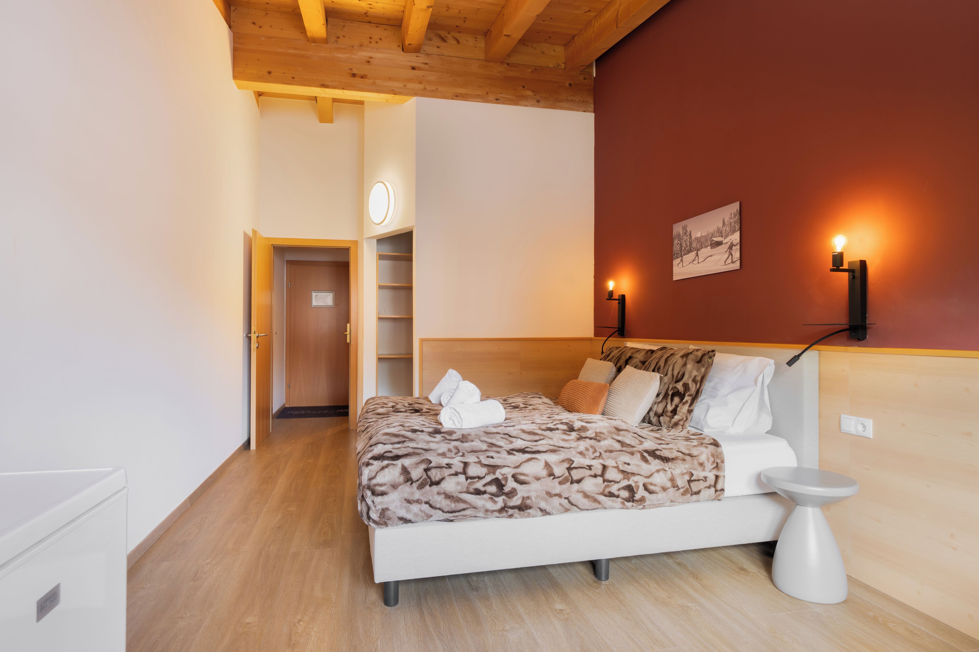 Ein Schlafzimmer mit Bett, Nachttisch, Wandlampen, einer Tür und einem Bild an der Wand.
