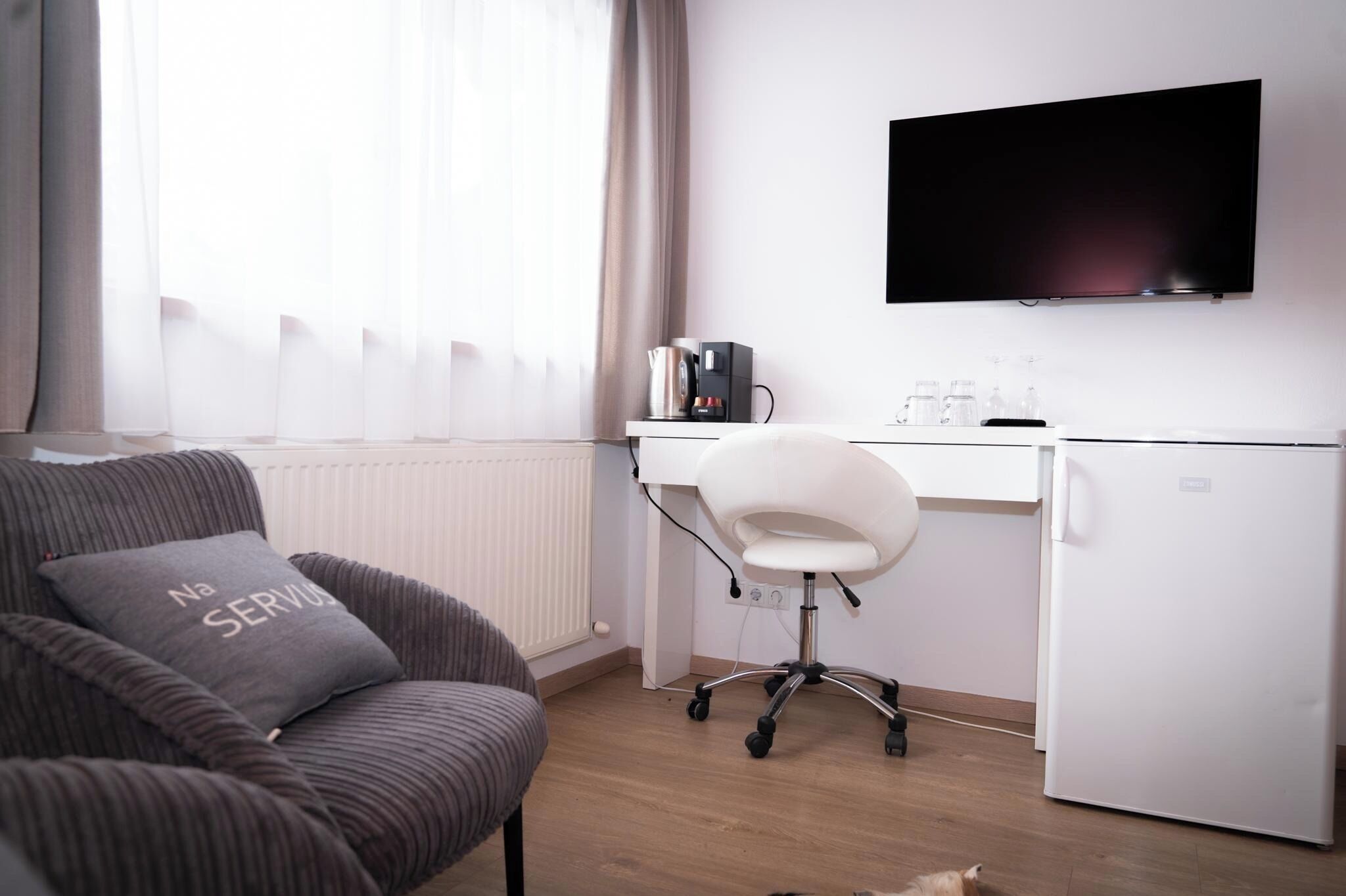 A modern room with a sofa, a desk, a television, and a refrigerator.