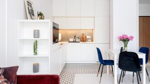 Une cuisine moderne avec des meubles blancs, un coin repas avec des chaises bleues et un canapé rouge.