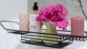Une étagère en métal noir sur laquelle sont posés un vase de fleurs roses, une bougie rose et deux flacons de lotion.