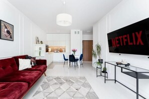 Una sala de estar moderna con un sofá rojo, una zona de comedor con sillas azules y una pantalla de televisión grande que muestra el logotipo de Netflix.