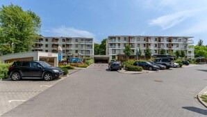 Un immeuble d’appartements moderne avec une entrée principale, plusieurs places de stationnement et un petit bâtiment portant l’inscription « CCC » sur le côté gauche.
