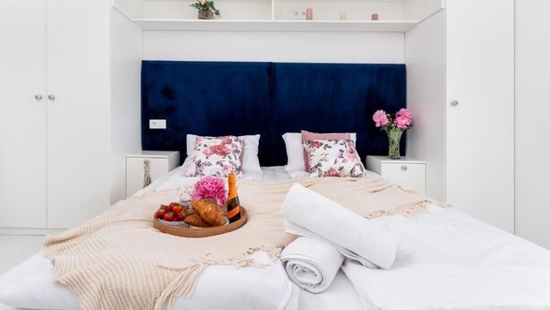 Une chambre à coucher bien rangée, avec un lit, deux tables de chevet, une commode et une étagère ornée d’objets décoratifs.