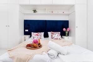 Une chambre à coucher bien rangée, avec un lit, deux tables de chevet, une commode et une étagère ornée d’objets décoratifs.