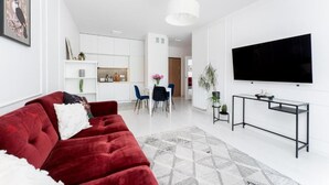 Un salon moderne avec un canapé rouge, un téléviseur et un coin repas comprenant des chaises et une table.