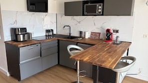 A compact kitchen with a built-in dishwasher, a coffee maker, a microwave, and a coffee grinder.