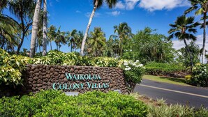 A sign for Waikoloa Colony Villas with a road leading to it, surrounded by lush greenery and palm trees. - 3BR Golf Course View Condo Waikoloa Colony Villas #805 - Vrkcv (Waikoloa)