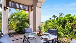 An outdoor patio with a table set for four, surrounded by chairs, and a view of greenery and palm trees. - 3BR Golf Course View Condo Waikoloa Colony Villas #805 - Vrkcv (Waikoloa)