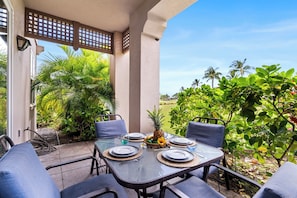 An outdoor patio with a table set for four, surrounded by chairs, and a view of greenery and palm trees. - 3BR Golf Course View Condo Waikoloa Colony Villas #805 - Vrkcv (Waikoloa)